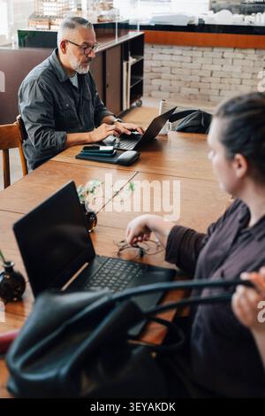 Male freelancer working on laptop while sitting at desk in shared workspace Stock Photo