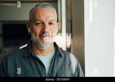 Portrait of smiling male entrepreneur wearing wireless in-ear headphones Stock Photo