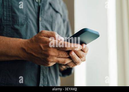 Midsection of male entrepreneur text messaging through smart phone at office Stock Photo