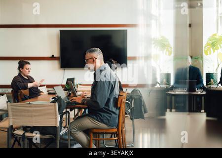 Male entrepreneur working on laptop while sitting on chair at shared working space Stock Photo