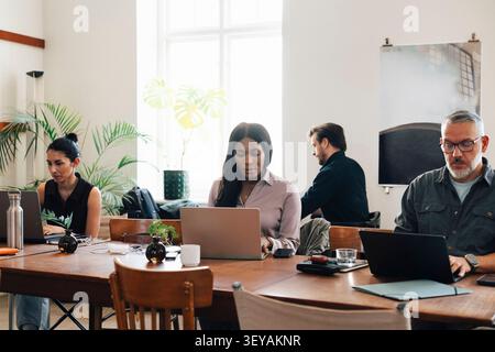 Diverse freelancers managing their tasks on laptops while working at shared open-plan workspace table Stock Photo