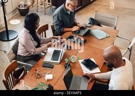 High angle view of freelancers using laptops and electronic gadgets while sitting at large table Stock Photo