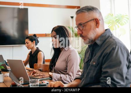 Female entrepreneur working on laptops while sitting with colleagues at shared working space Stock Photo