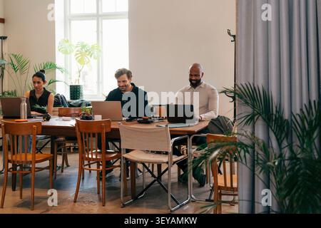 Group of male and female freelancers working side by side while sitting at coworking space table Stock Photo
