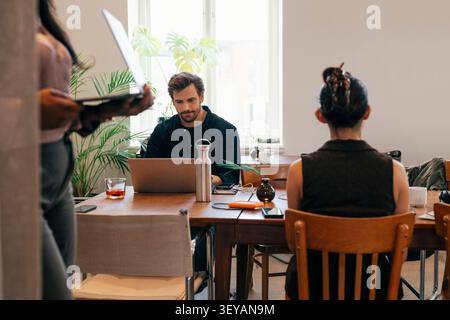 Male entrepreneur working on laptop while sitting at wooden desk in modern working space Stock Photo