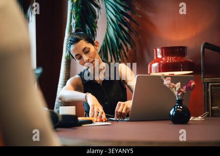 Businesswoman connecting external hard drive to her laptop while sitting at desk in coworking lounge Stock Photo