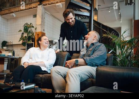 Happy coworkers laughing together while sitting on couch in modern office lounge Stock Photo