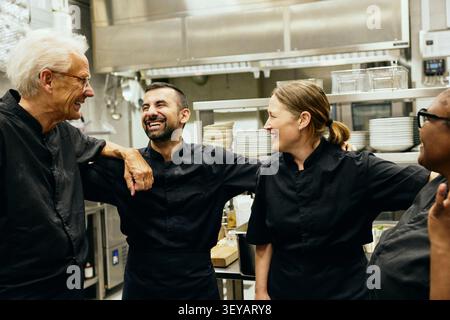 Group of professional restaurant chefs laughing while talking with each other in kitchen Stock Photo