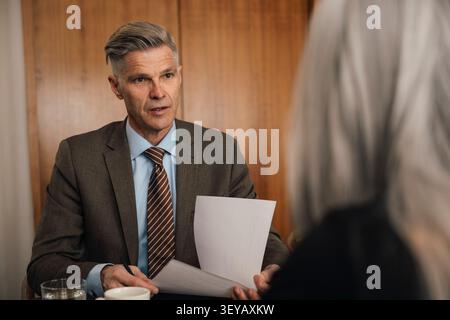 Senior businessman having conversation with his colleague while reviewing documents at office Stock Photo