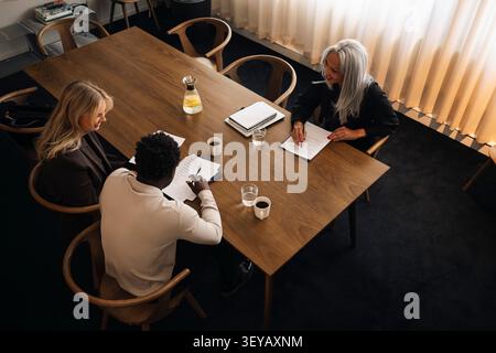 High angle view of diverse team reviewing documents with coffee in corporate boardroom Stock Photo