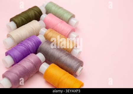 Colorful sewing thread spools neatly arranged on a pastel pink background with soft lighting and generous copy space for design, sewing supplies, craf Stock Photo