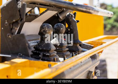 Ergonomic operator controls featuring black rubberized joysticks installed in yellow industrial machinery designed for precise construction tasks and Stock Photo