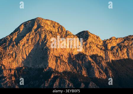 Golden sunlight illuminates rugged mountain peaks under clear blue sky Stock Photo