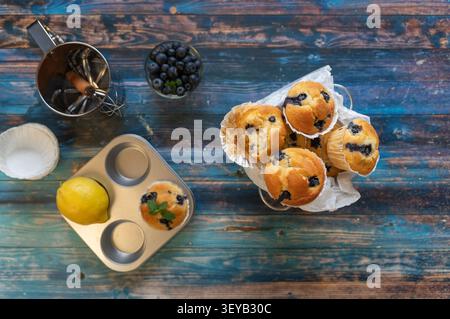 Homemade blueberry muffins arranged with fresh blueberries and baking ingredients on rustic table Stock Photo