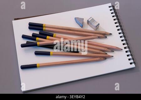 Several pencils arranged casually on a white sketch notebook with an eraser and sharpener. Stock Photo