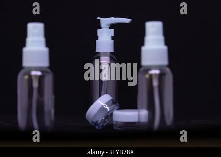 Three empty bottles are shown. One has a pump dispenser, and two have spray tops. The bottles are clear and arranged on a dark surface without any lab Stock Photo