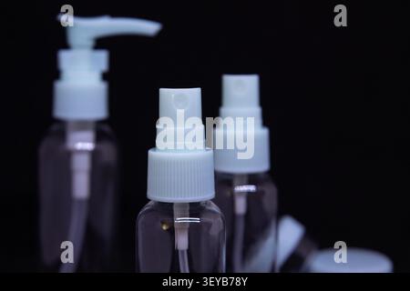 Three clear plastic bottles with pump dispensers and spray tops are placed close together against a dark backdrop. These bottles are empty and ready f Stock Photo