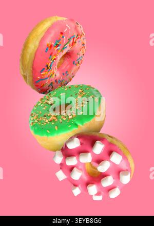 Tasty donuts covered with icing falling on pink background Stock Photo