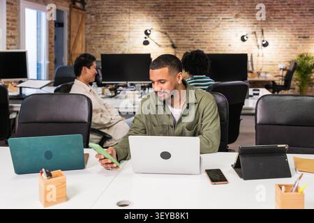 Focused young manager working on laptop and smartphone in modern office Stock Photo