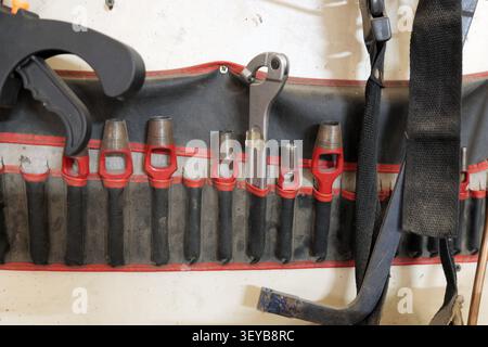 Workshop tools organized in a hanging roll, displaying various leather punches, a wrench, and other equipment, all ready for manual labor and maintena Stock Photo