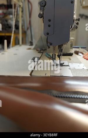 Industrial sewing machine performing stitching on brown leather material, fabricating a product with meticulous detail and precision in a manufacturin Stock Photo