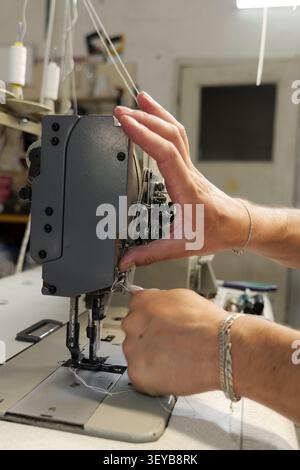 Hands carefully threading an industrial sewing machine, managing white thread and needles during the detailed process of preparing for production in a Stock Photo