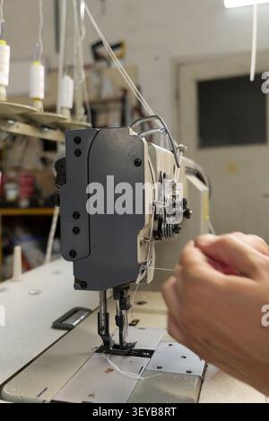Skilled hands carefully threading white cotton onto an industrial sewing machine, preparing for textile work in a garment factory or workshop, highlig Stock Photo