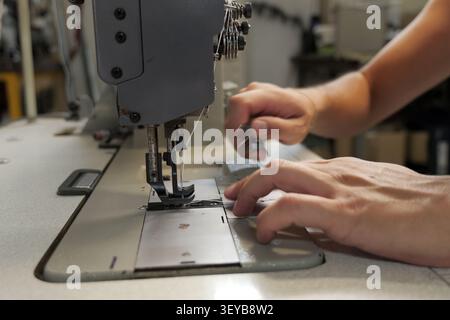 Professional tailor hands carefully guiding a piece of fabric under the needle of an industrial sewing machine, performing a precise stitch in a texti Stock Photo