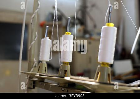 White thread spools are standing on a multiple thread stand, ready for use on an industrial sewing machine, representing precision in textile craftsma Stock Photo