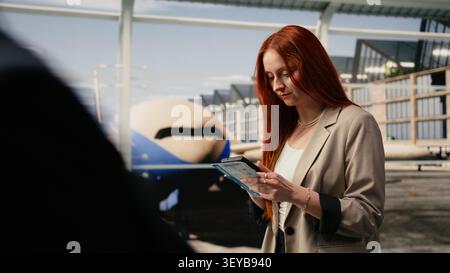 Female traveler in airport terminal taking photos with smartphone to boarding pass. Woman takes picture of flight details before departure, using phone camera to do travel document backup Stock Photo