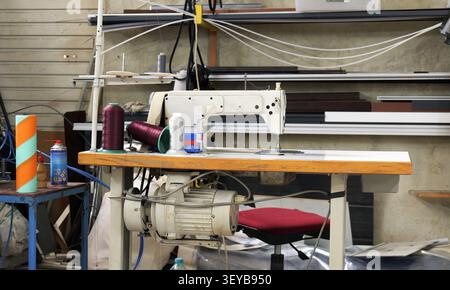 Industrial sewing machine standing on a wooden table, featuring colorful spools of thread and various equipment, ready for manufacturing garments in a Stock Photo