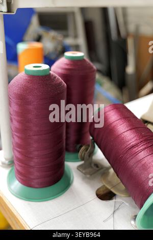 Burgundy thread bobbins winding on an industrial sewing machine in a textile workshop, showcasing supplies and equipment for garment production and ta Stock Photo