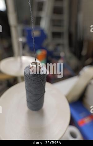 Gray thread unwinding from a spool on an industrial machine, highlighting the process of textile manufacturing and the continuous flow of production i Stock Photo