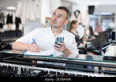 Upset man store owner make calculations, check documents and counts budget deficit using her phone Stock Photo