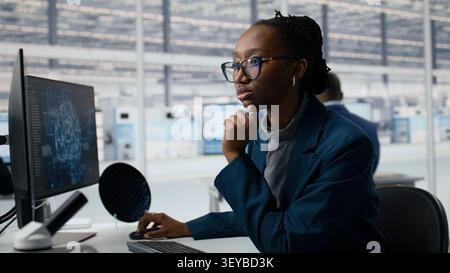 Examining microchip circuit layout, artificial intelligence and developer in factory RD office. Using AI tech, semiconductors manufacturing and African american employee, camera A Stock Photo