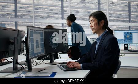 Asian man using artificial intelligence in microchip factory office to optimize hardware. Senior manager training AI model in RD in research lab, improving manufacturing efficiency, camera A close up Stock Photo