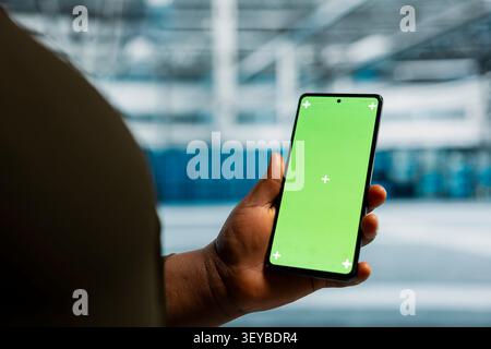 Data center administrator works with a chroma key smartphone, using an editable screen to review performance data. Stock Photo