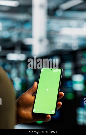 Data center programmer works with a chroma key smartphone, using an editable screen to review performance data. Stock Photo