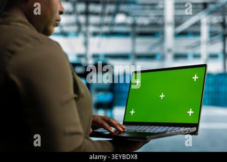 Team supervisor uses a green screen laptop in a data center for cyber threat response, screen replacement, and server workflow monitoring. Stock Photo