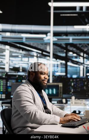 Positive server facility IT expert works with workstation to update servers tech, setting up equipment working with software. Stock Photo