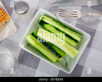 On table there is plate with summer snack - long pieces of cucumber pulp Stock Photo