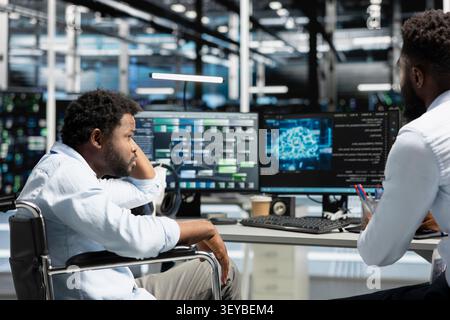 Data center manager and wheelchair user use a computer to manage machine learning workloads, working with AI technology and high performance systems. Stock Photo