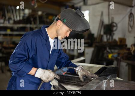Young man welding metal part in workshop Stock Photo