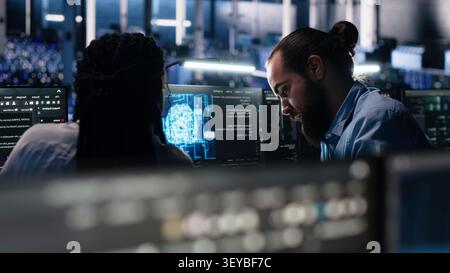 Server facility admin teaching trainee to check AI network working with AI. IT expert and African American woman at work applying AI to supervise servers powering ML. Stock Photo