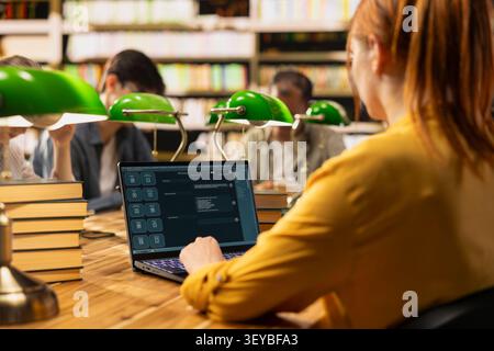Student using AI study assistant interface on laptop during group study session in library, showcasing modern education with generative AI tools. Learning scene with classmates at table. Stock Photo