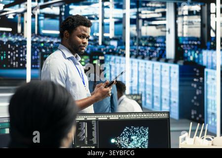 African American technician reviews an AI dashboard in a server hub to find performance issues and reduce hardware failures. Stock Photo