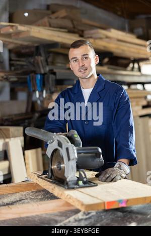 Working at sawmill - man saws wooden board using circular saw Stock Photo