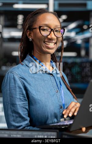 Friendly IT technician in data infrastructure center tracking system operational performance. Stock Photo