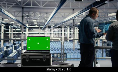 Programmers use green screen laptop in a data center to deploy deep learning software and support AI workloads. Stock Photo