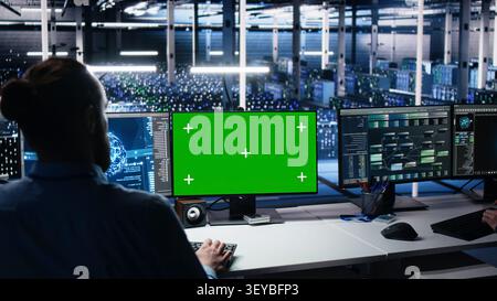 Data center engineer uses green screen PC in a server room to monitor AI diagnostics and neural network performance. Stock Photo